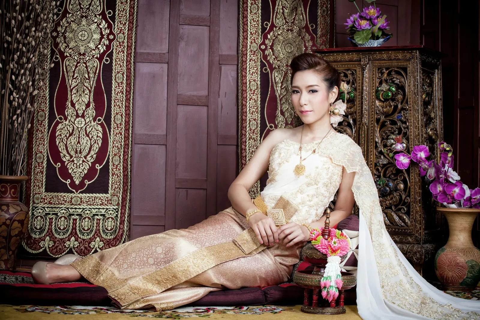 Woman in a gold Thai traditional costume in front of the prang of Wat Arun in Bangkok
